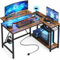 Bestier rustic brown L-shaped computer desk with a metal base, shelves, hooks and strip lighting.